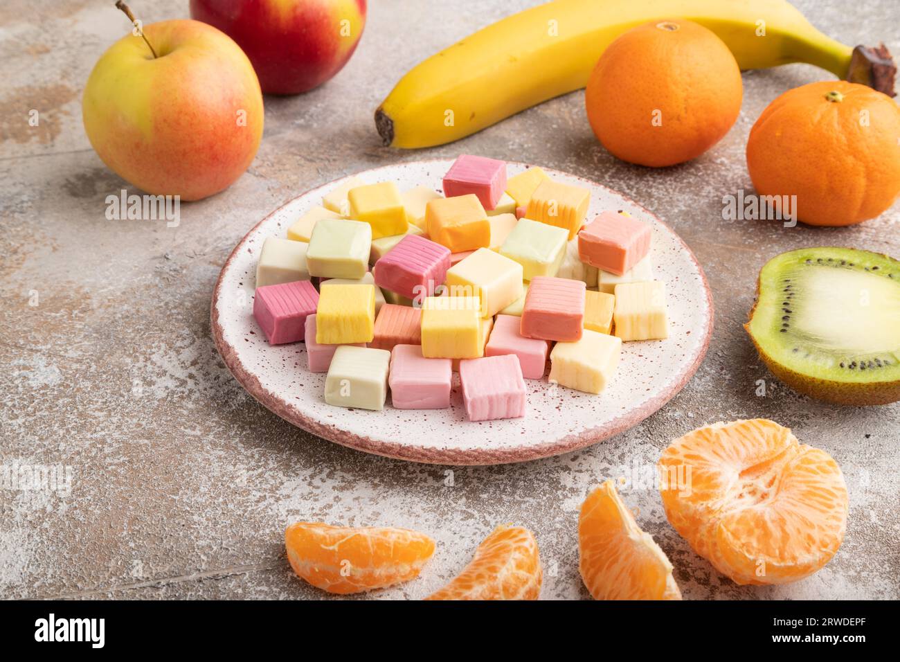 Various fruit jelly chewing candies on plate on brown concrete background. apple, banana, tangerine, side view, close up. Stock Photo