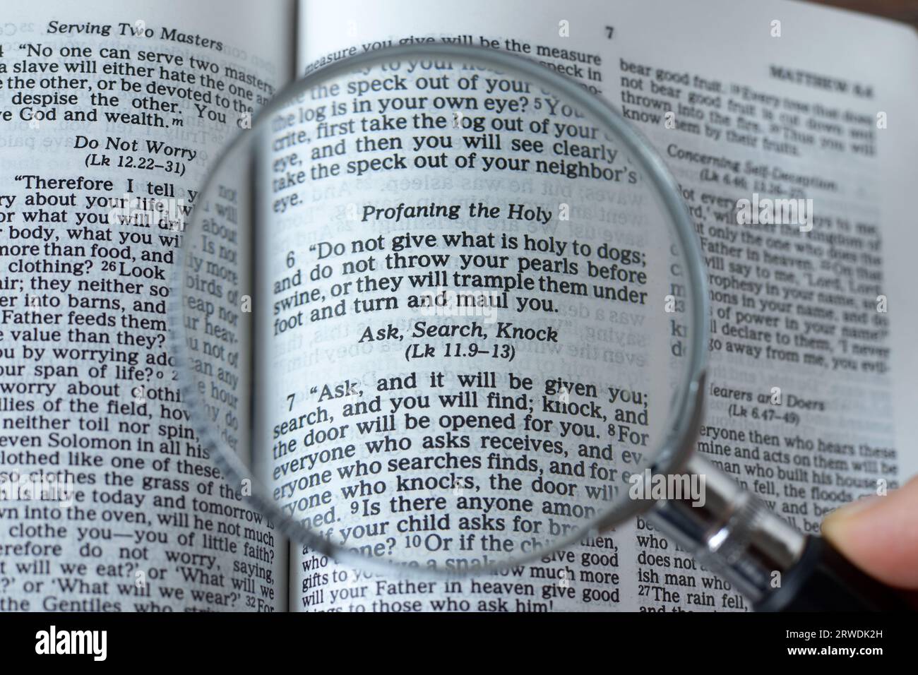 Ask, search, knock, biblical text verse. Human hand holding a magnifying glass over Holy Bible Book. Close-up. Stock Photo