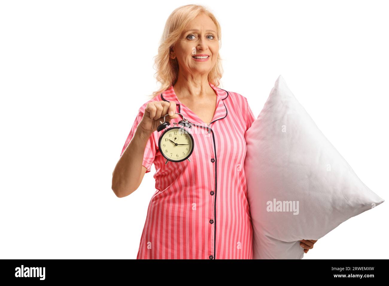 Beautful mature woman in pajamas holding a pillow and alarm clock isolated on white background Stock Photo