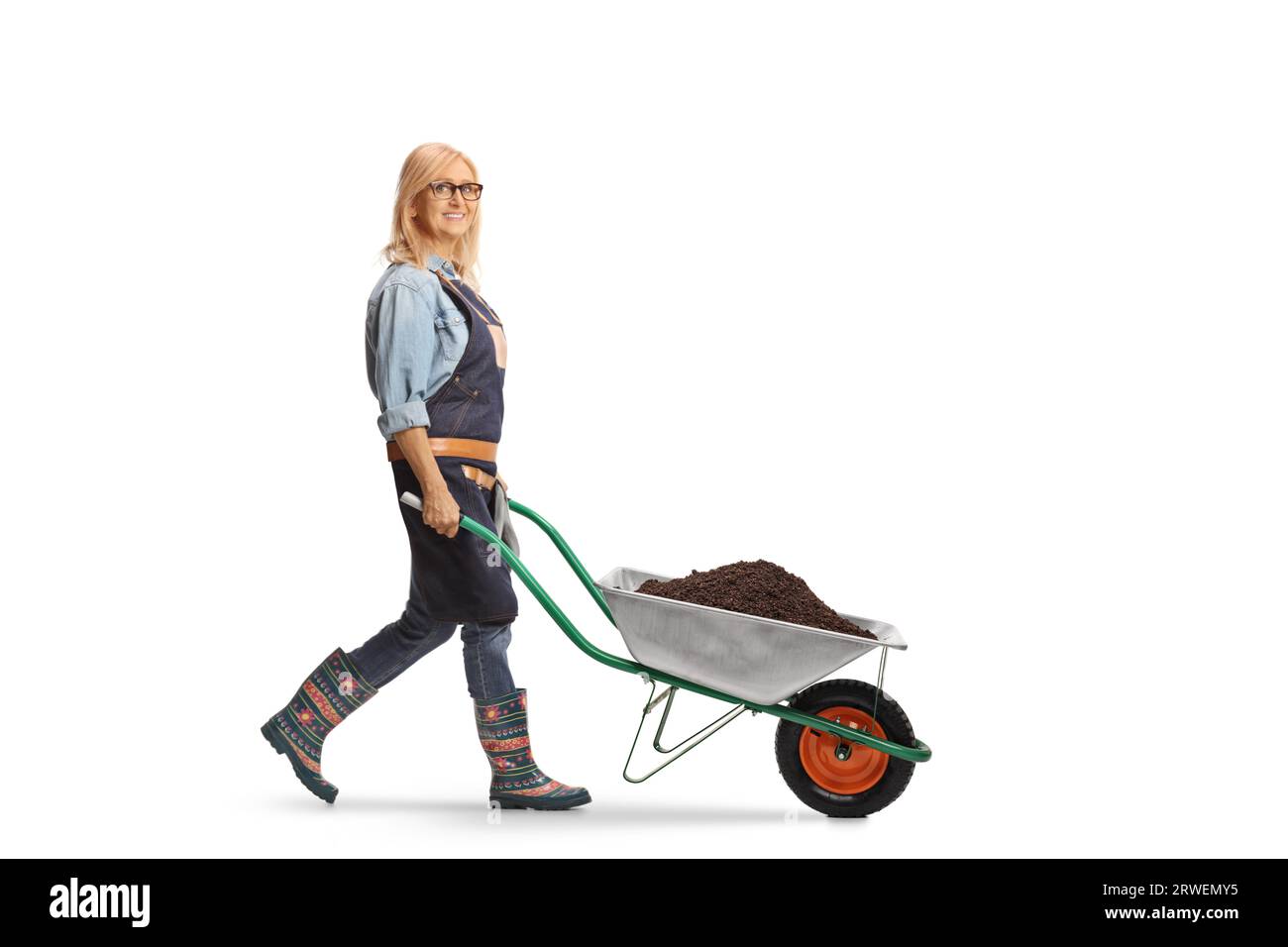 Female farmer walking with a wheelbarrow full of soil and looking at camera isolated on white background Stock Photo