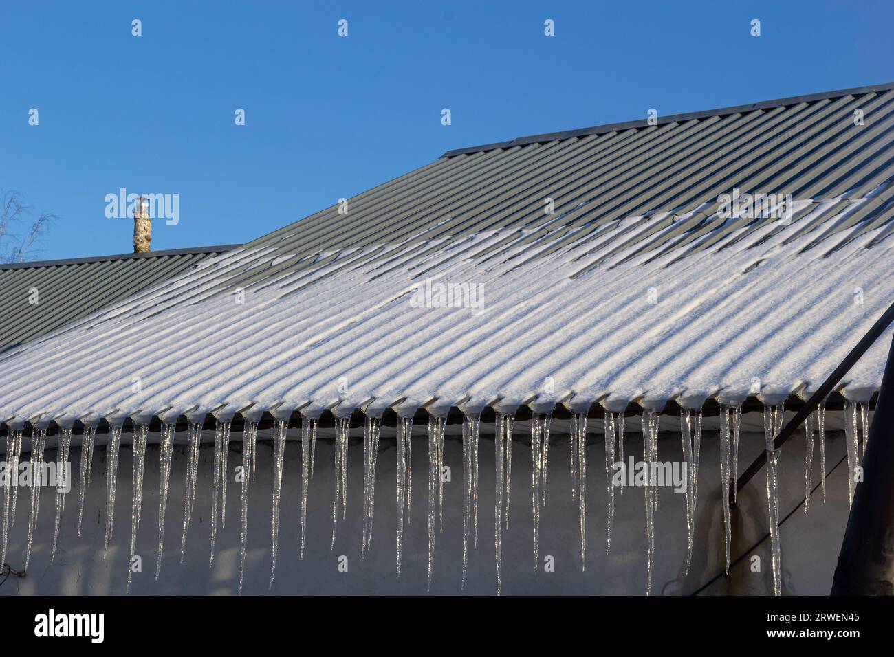 Sharp icicles and melted snow hanging from the eaves of the roof. Beautiful transparent icicles slowly gliding of a roof. Stock Photo