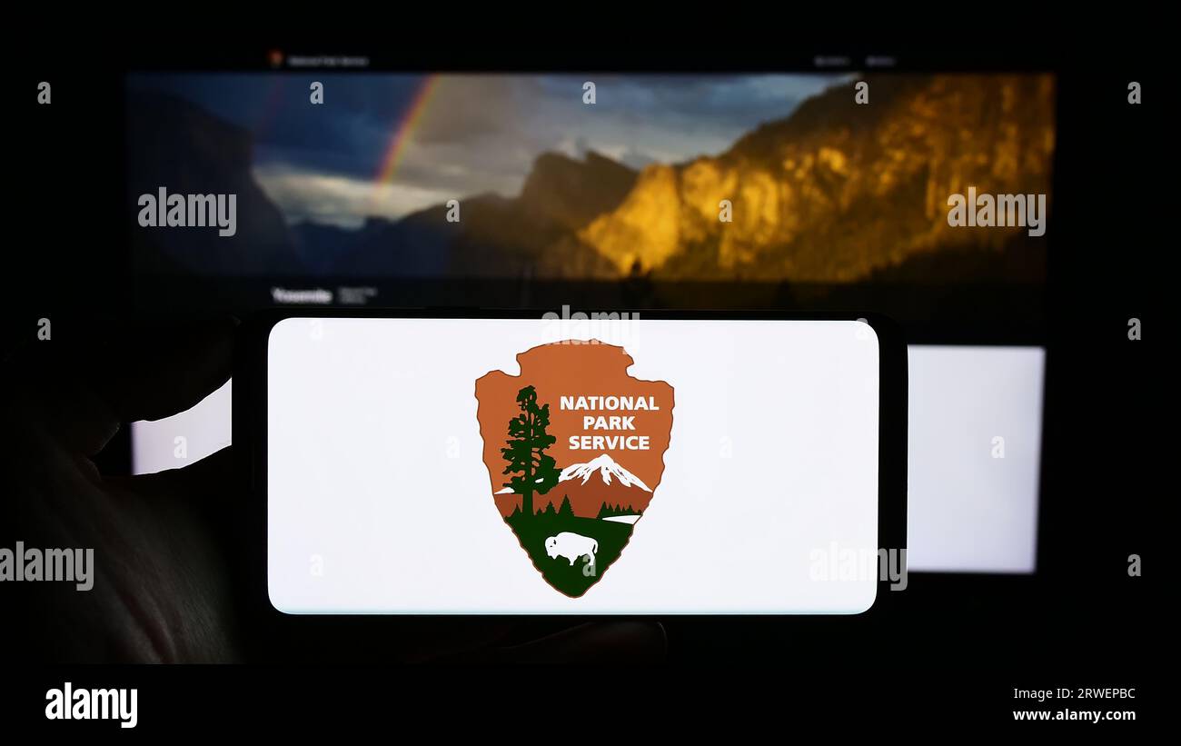 Person holding smartphone with logo of US agency National Park Service (NPS) on screen in front of website. Focus on phone display. Stock Photo