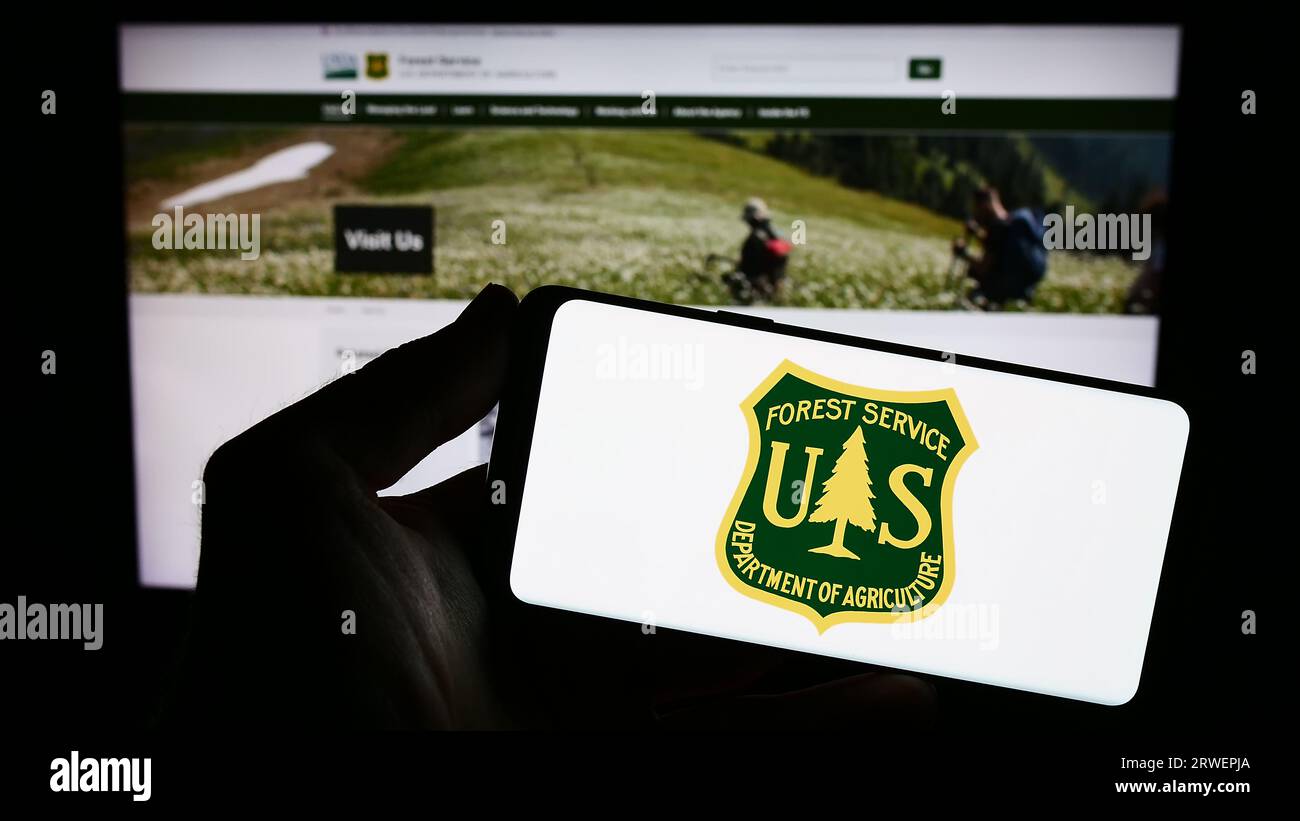 Person holding smartphone with logo of United States Forest Service (USFS) on screen in front of website. Focus on phone display. Stock Photo