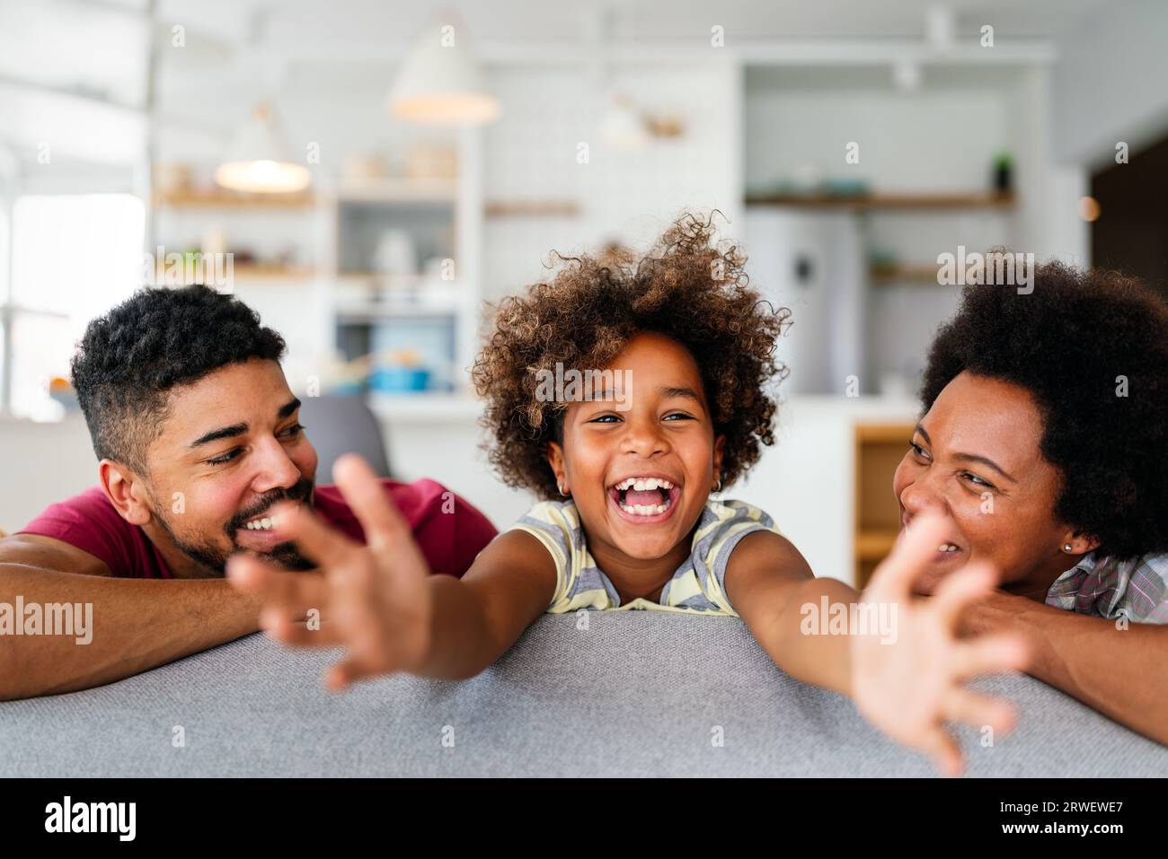 Happy biracial girl smiling with young multiracial parents enjoy weekend at home together, Stock Photo