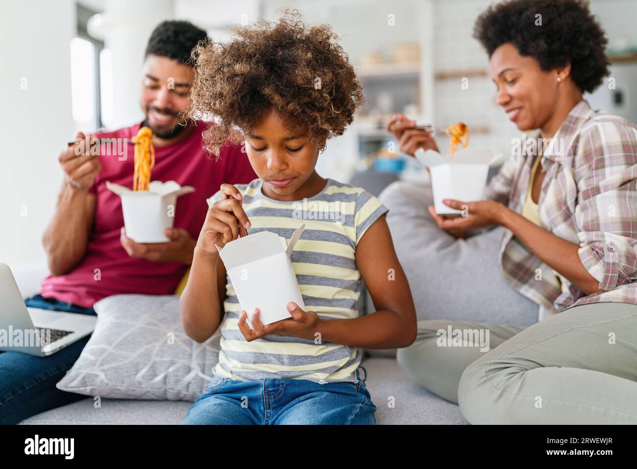 Happy african family eating at living room and enjoying time together. Home delivary takeaway food Stock Photo