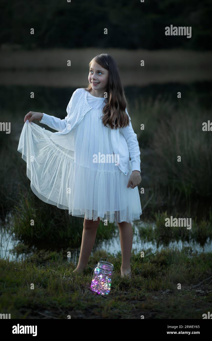 Full length portrait of a young girl dressed in a white dress at dusk Stock Photo