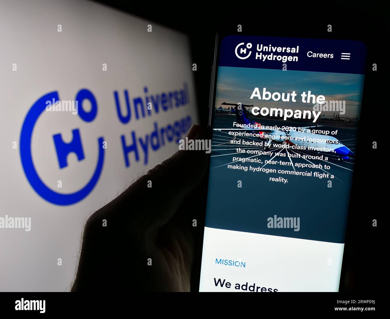 Person holding cellphone with webpage of US aerospace company Universal Hydrogen Co. on screen in front of logo. Focus on center of phone display. Stock Photo