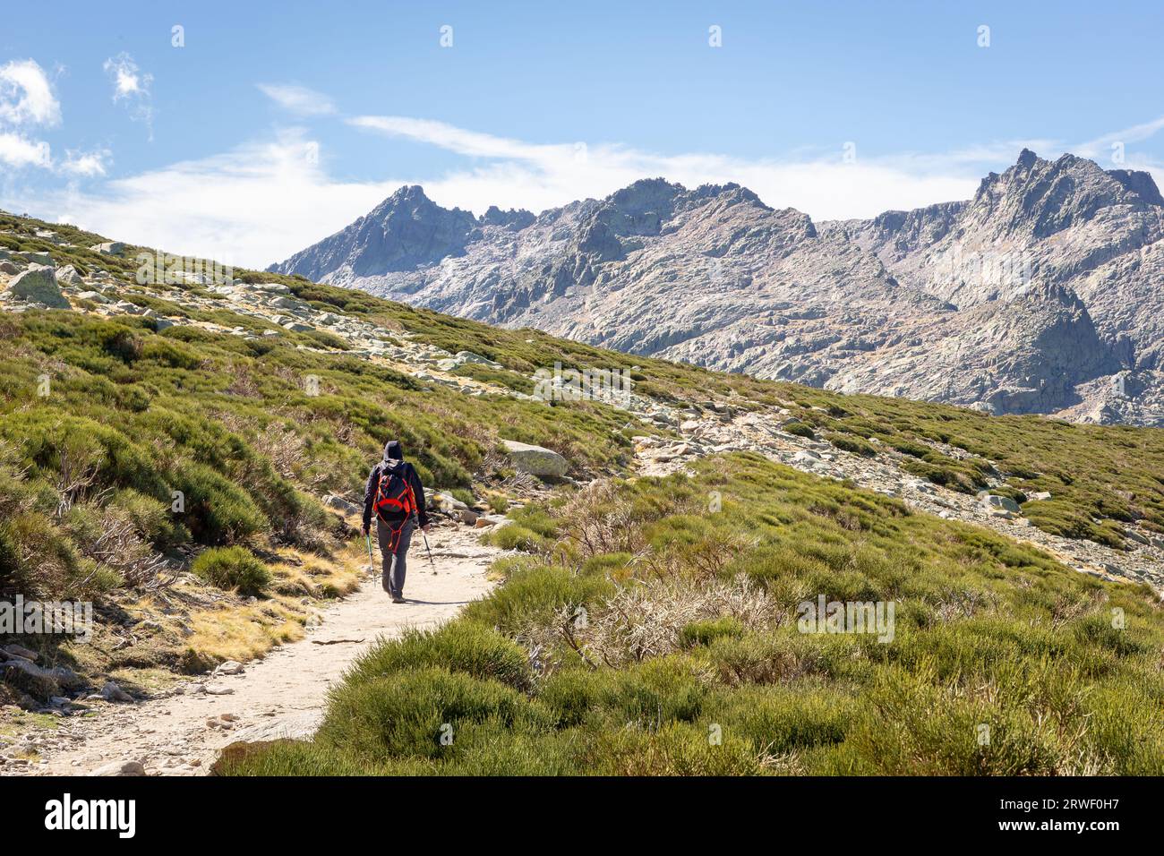 Tourist hiking on a dirt trail to the Laguna Grande de Gredos lake from the Plataforma de Gredos in Sierra de Gredos mountains, dry brown grass, Spain. Stock Photo
