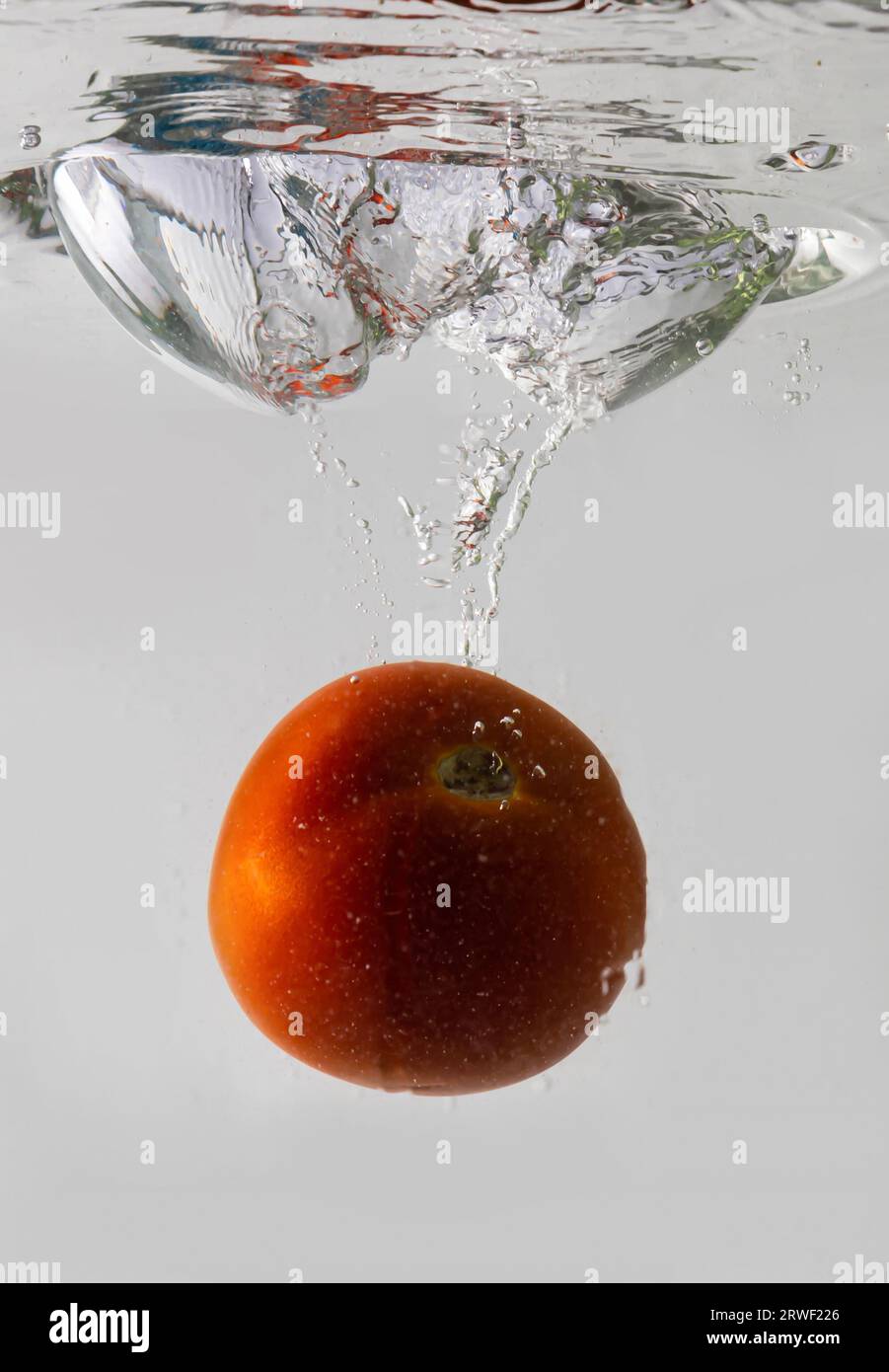 Ripe tomato falls deeply under water with a big splash. Stock Photo