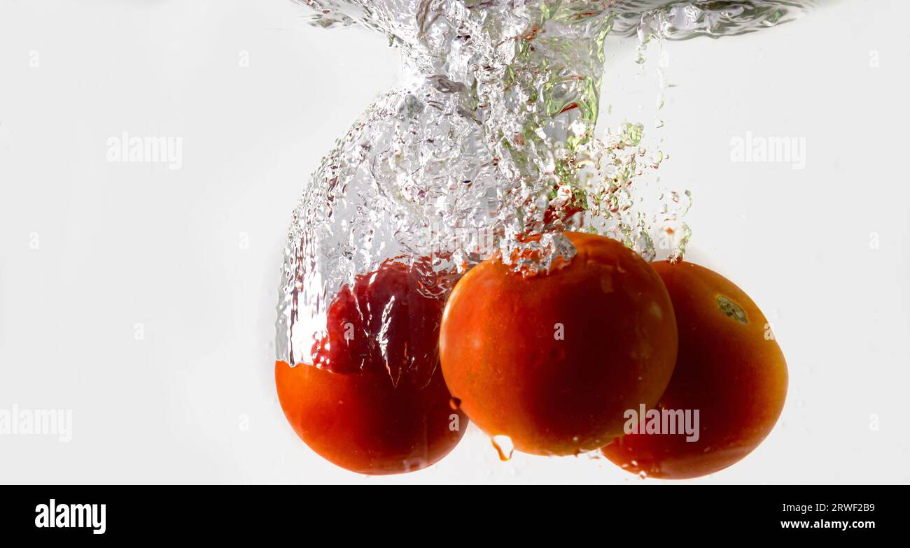 Ripe tomato falls deeply under water with a big splash. Stock Photo