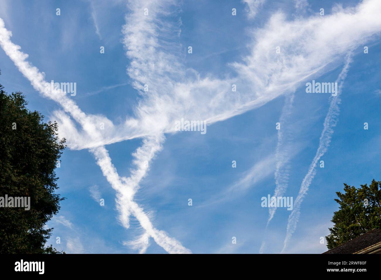 White criss-cross vapour trails from Heathrow bound aircraft forming triangular patterns against a blue sky in Surrey, south-east England Stock Photo