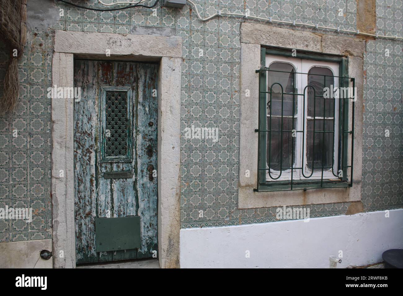 Vintage looking Front Door with Distressed Paintwork and Window patterned Metal Grill, surrounded with Green& White Patterned Portuguese Wall Tiles. Stock Photo