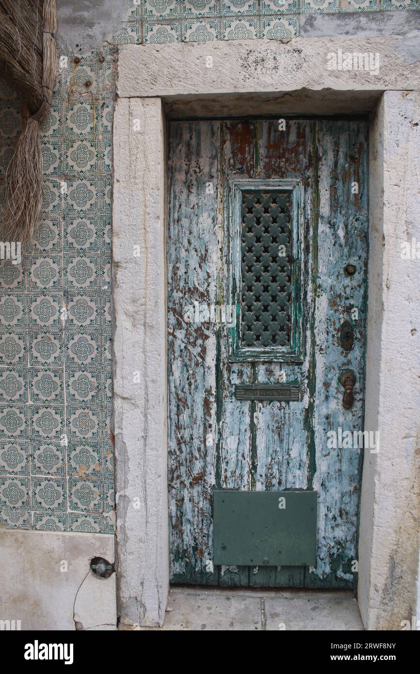A Vintage looking Front Door with Distressed Paintwork and patterned Metal Grill, surrounded with Green and White Patterned Portuguese Wall Tiles. Stock Photo
