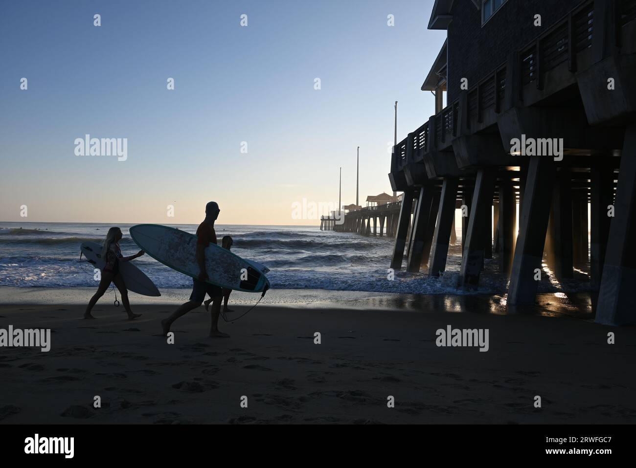 Surfers carry their boards along the beach during an early morning of surfing off of Jennette's Pier in Nags Head, North Carolina. Stock Photo
