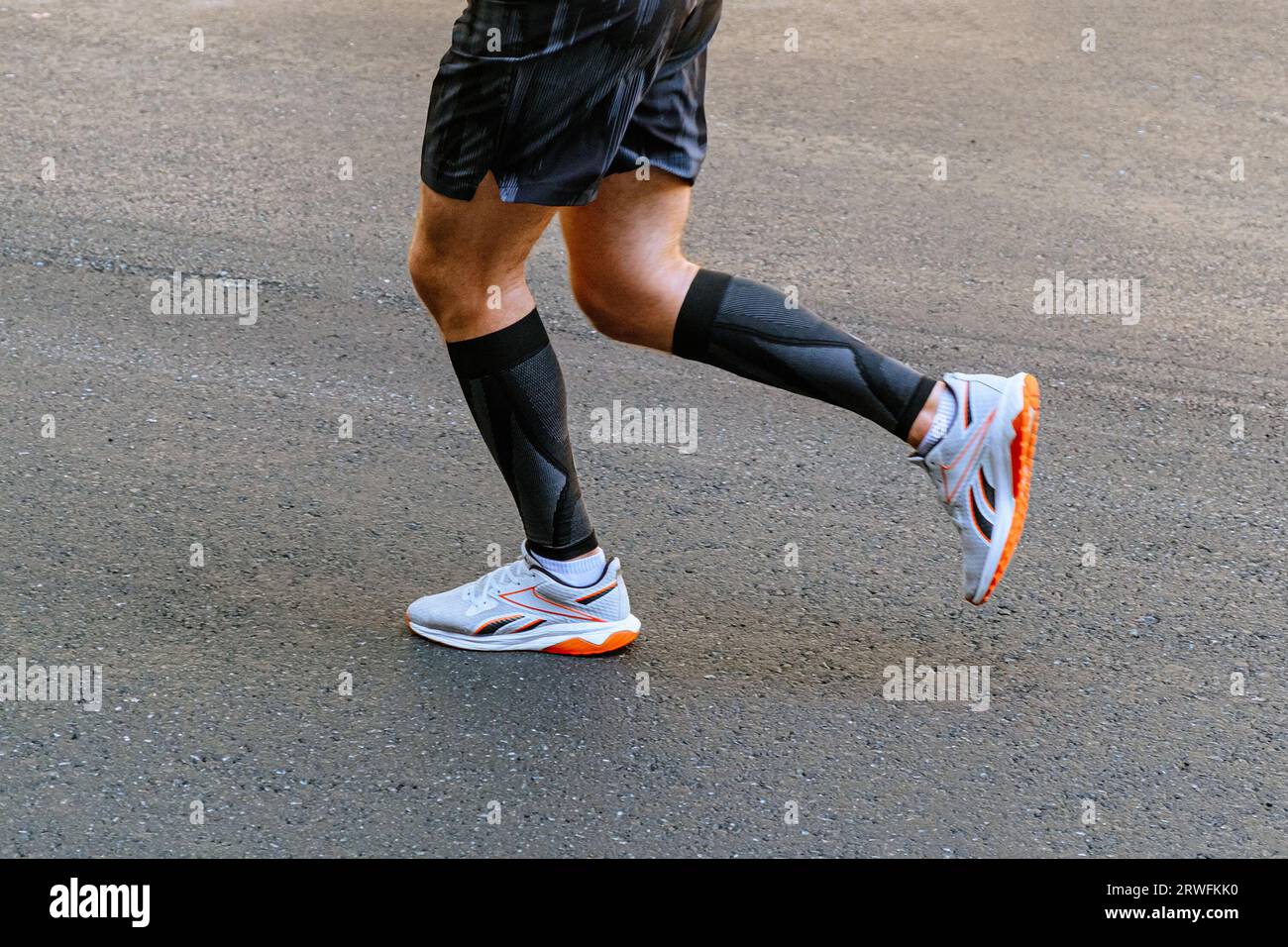 legs male runner in black compression sleeves running on asphalt road