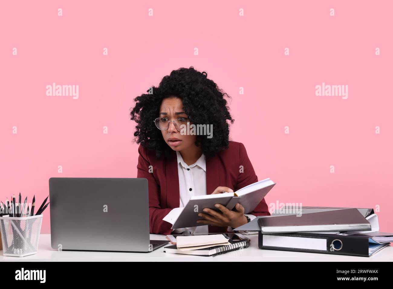 Stressful deadline. Tired woman working at white desk against pink background Stock Photo