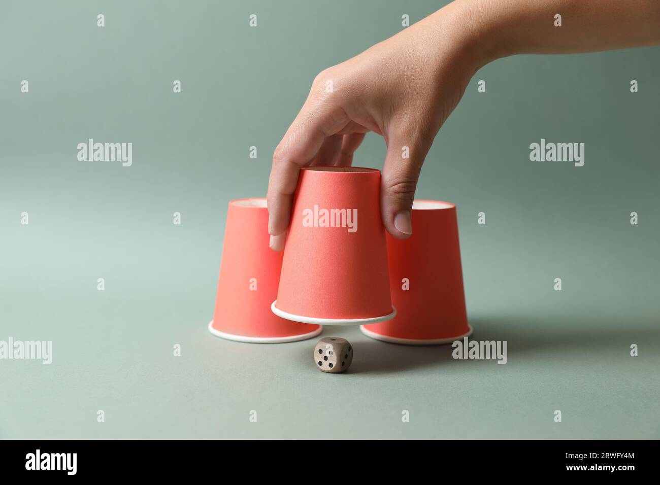Woman showing dice under cup on pale olive background, closeup ...