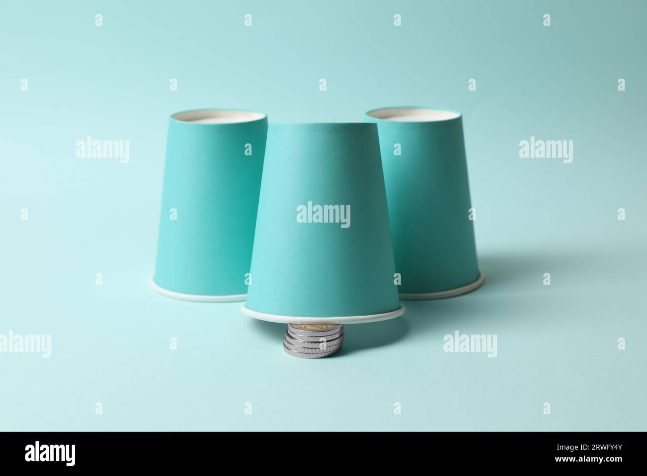 Three paper cups and coins on light blue background. Thimblerig game ...