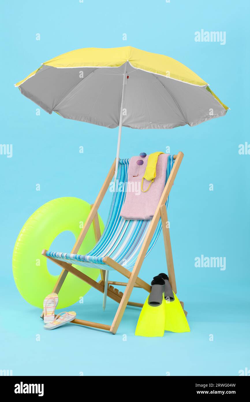 Deck chair, umbrella and beach accessories against light blue ...