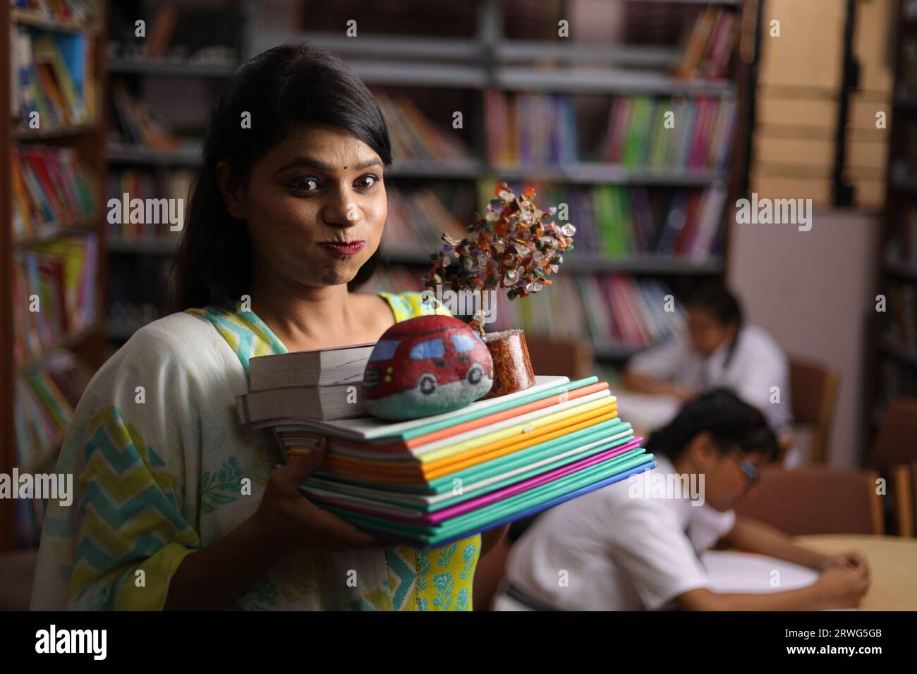 Indian teacher holding a bundle books in her hands, standing in library, study pressure, education force. Stock Photo