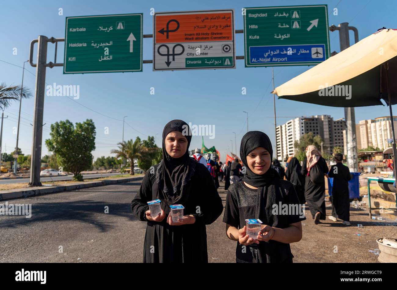 Iraqi Shia girls distribute water among Shia Muslim pilgrims marching from Najaf towards Shrine city of Karbala. Every year, millions of Shia Muslims and some from other faiths undertake a 20-day pilgrimage on foot from various cities in Iraq and Iran to the holy city of Karbala. This pilgrimage is in remembrance of Imam Hussein, the grandson of the Prophet Muhammad, who died in a battle in 680 AD. On the 40th day of mourning for Hussein, known as Arbaeen, pilgrims converge in Karbala to pay tribute at his shrine. Along the way, volunteers provide food, water, and shelter, and villagers open t Stock Photo