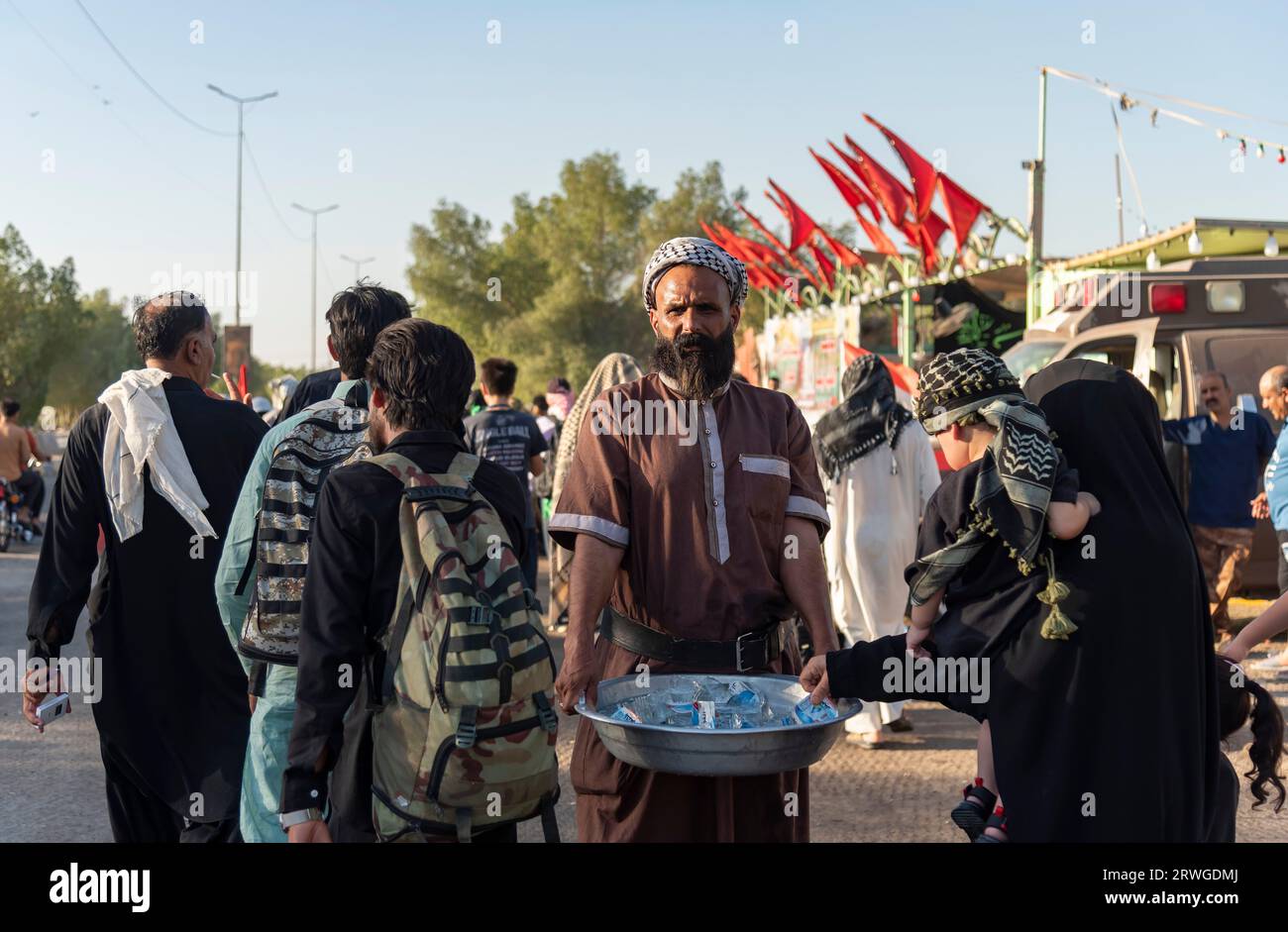 An Iraqi man distribute water among Shia Muslim pilgrims marching from Najaf towards Shrine city of Karbala. Every year, millions of Shia Muslims and some from other faiths undertake a 20-day pilgrimage on foot from various cities in Iraq and Iran to the holy city of Karbala. This pilgrimage is in remembrance of Imam Hussein, the grandson of the Prophet Muhammad, who died in a battle in 680 AD. On the 40th day of mourning for Hussein, known as Arbaeen, pilgrims converge in Karbala to pay tribute at his shrine. Along the way, volunteers provide food, water, and shelter, and villagers open their Stock Photo