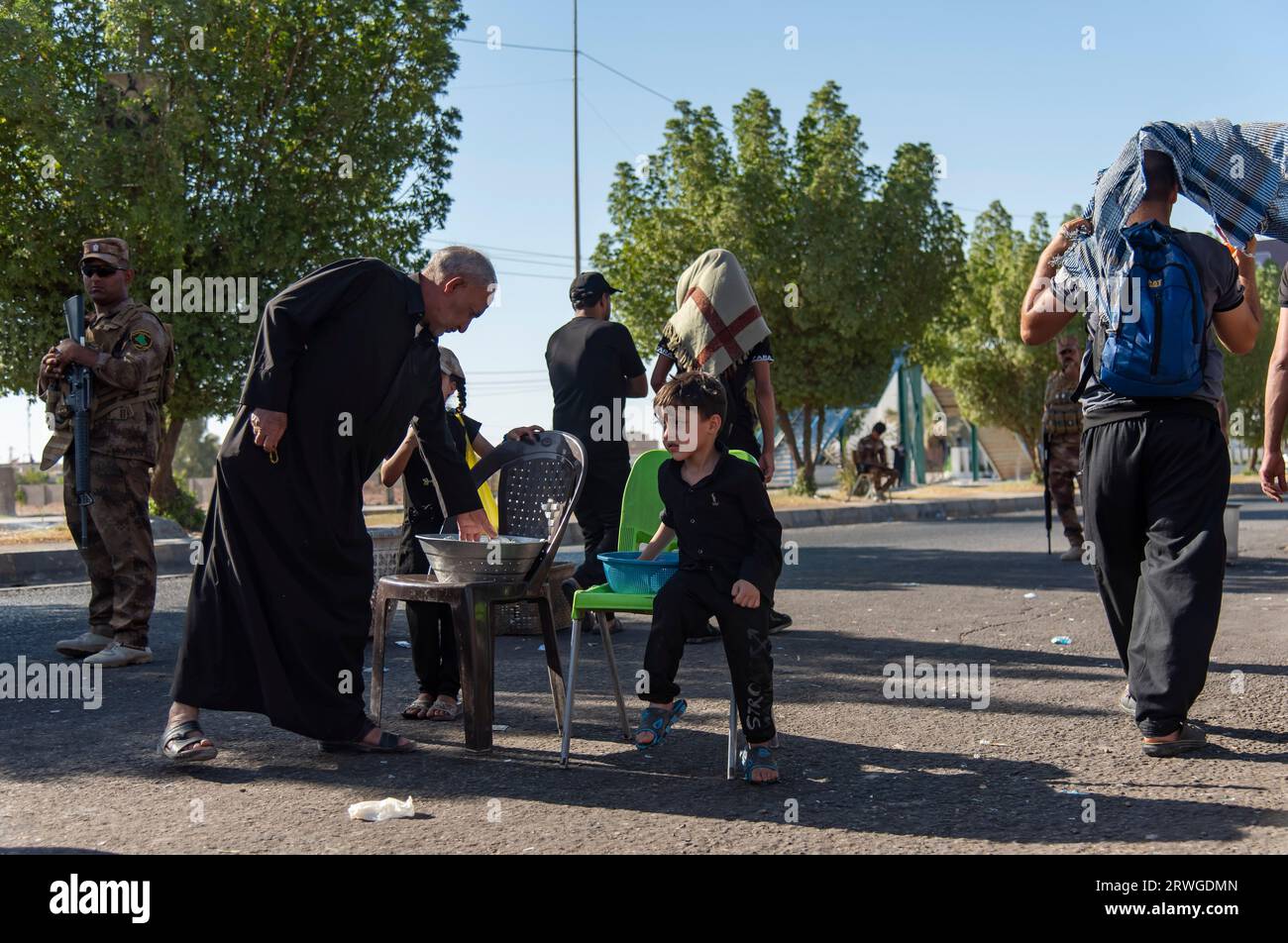 Iraqi Shia kids distribute water among Shia Muslim pilgrims marching from Najaf towards Shrine city of Karbala. Every year, millions of Shia Muslims and some from other faiths undertake a 20-day pilgrimage on foot from various cities in Iraq and Iran to the holy city of Karbala. This pilgrimage is in remembrance of Imam Hussein, the grandson of the Prophet Muhammad, who died in a battle in 680 AD. On the 40th day of mourning for Hussein, known as Arbaeen, pilgrims converge in Karbala to pay tribute at his shrine. Along the way, volunteers provide food, water, and shelter, and villagers open th Stock Photo