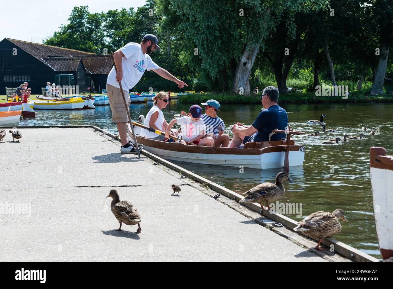 A family of a mother and father and their two children board a row boat at Thorpeness Meare Suffolk in late summer. Stock Photo