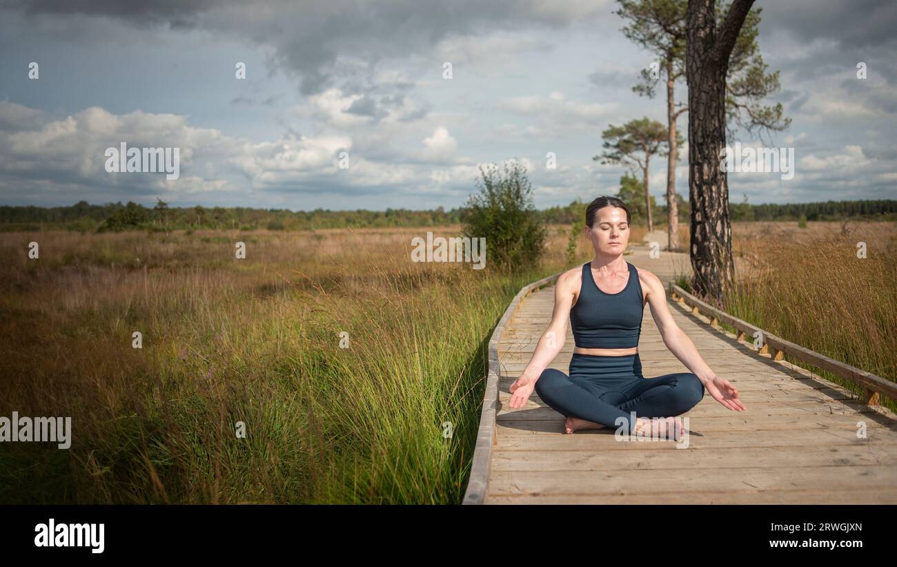 woman sitting on a boardwalk meditating and practicing yoga Stock Photo