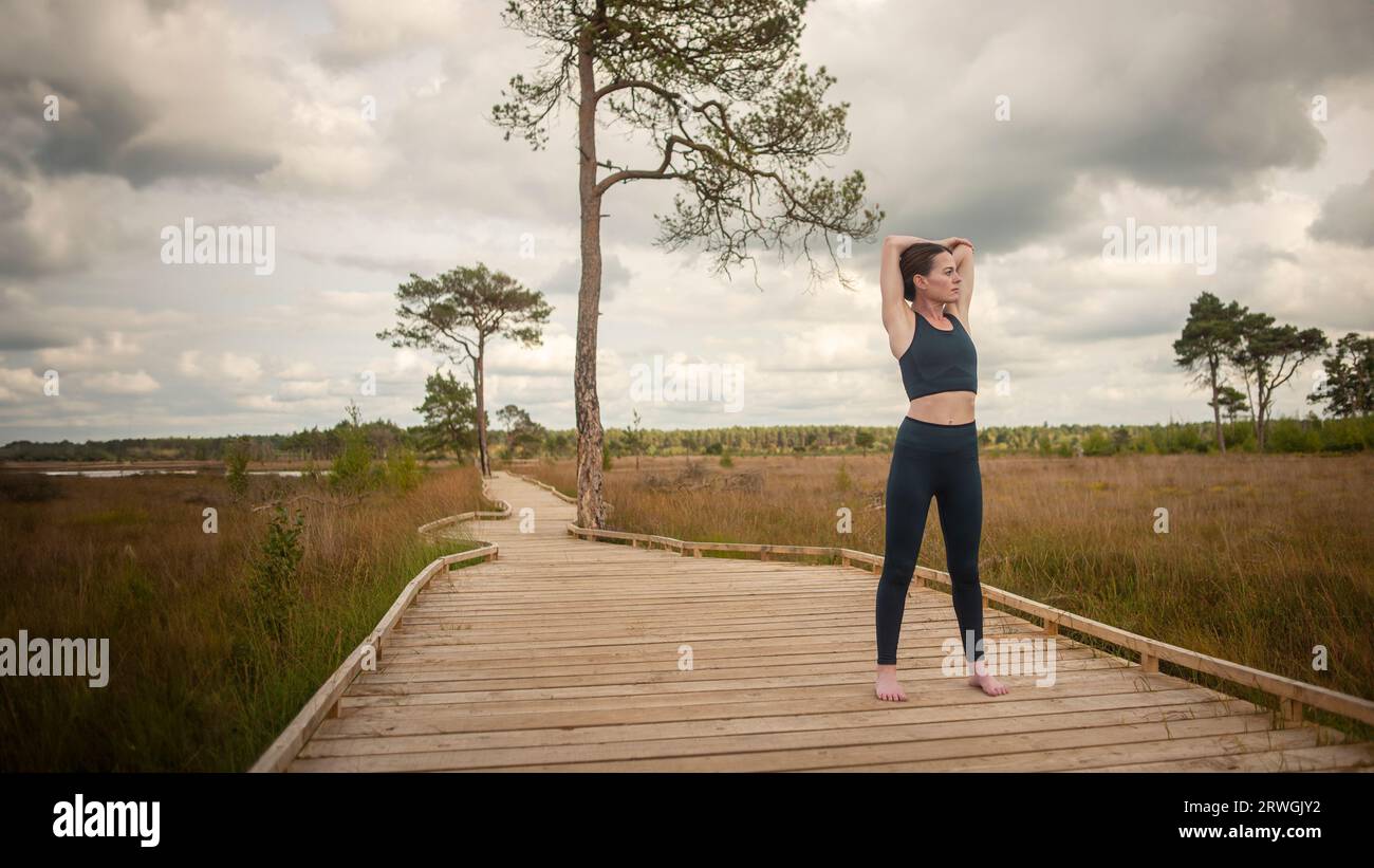 Fit, sporty woman doing an arm stretch exercise outside on a boardwalk Stock Photo