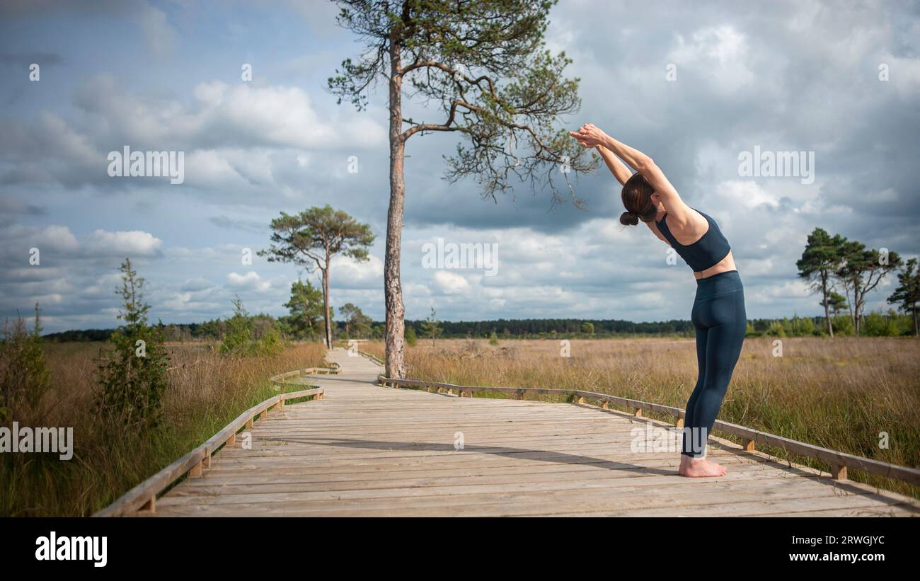 Fit, sporty woman practicing yoga on a boardwalk, doing a backbend. Stock Photo