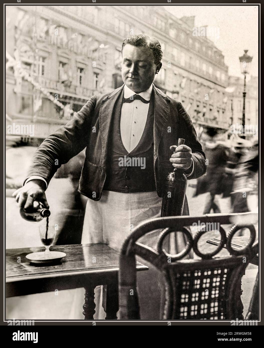 Paris Waiter Wine 1900s Vintage Retro Classic historic french waiter B&W serving wine at street cafe restaurant boulevard bistro wearing typical french waiter uniform, pouring a glass of red wine outside cafe brasserie table alfresco reportage Paris France Stock Photo