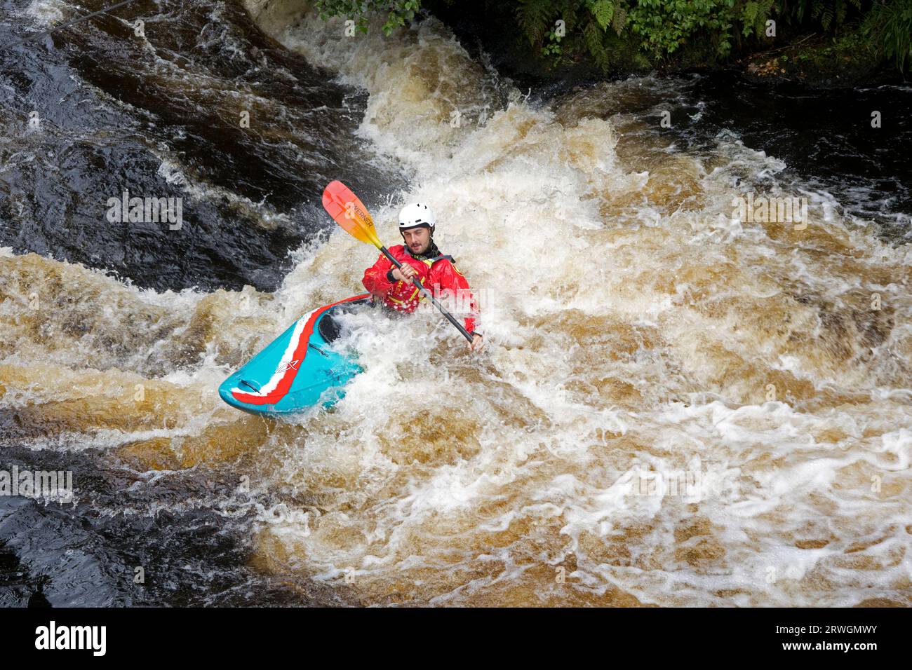 Canoeist in red jacket and crash helmet in blue canoe riding the rapids Whitewater slalom canoeing  in River Tryweryn at he National Whitewater Centre Stock Photo