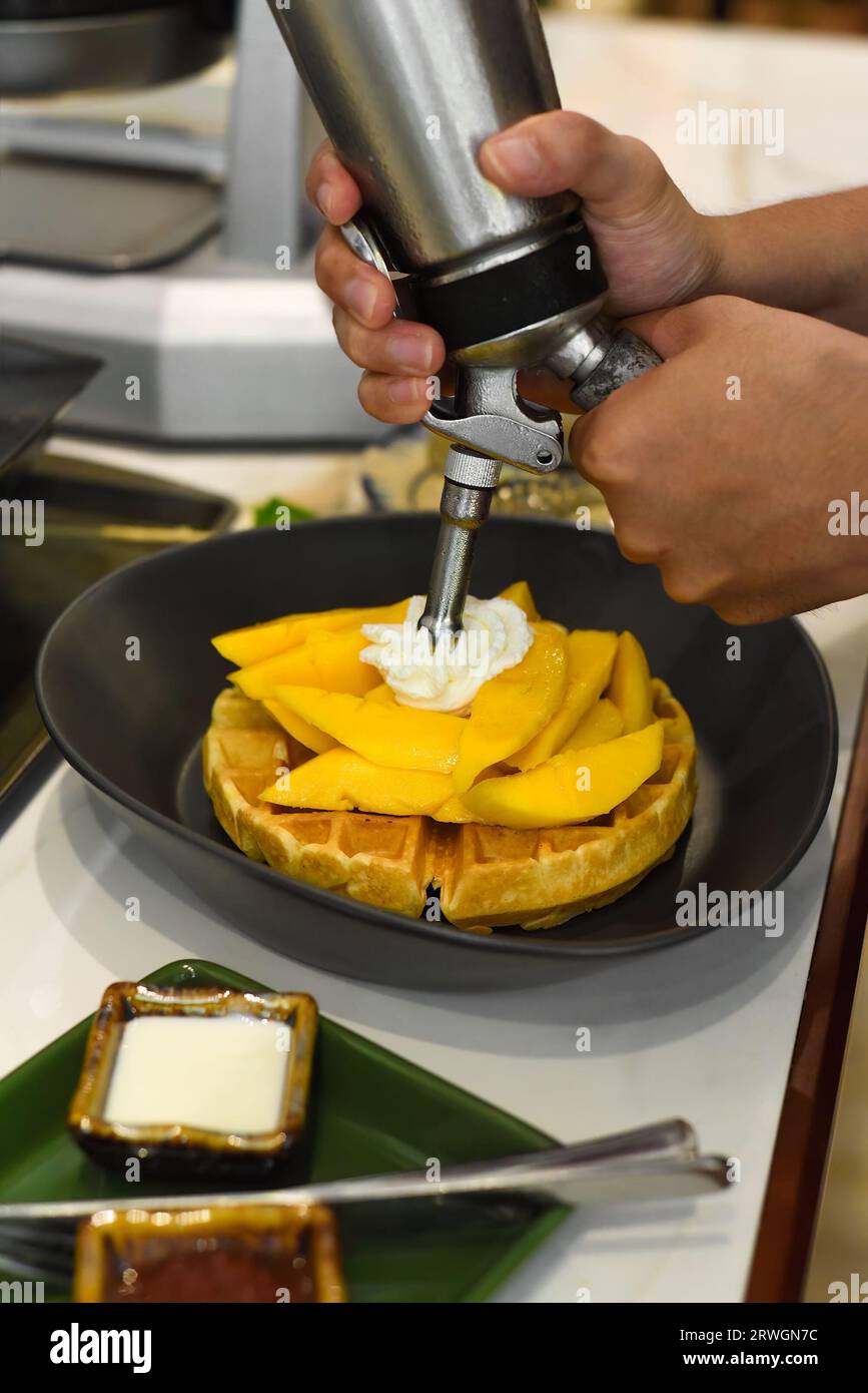 Chef adding fresh cream on sliced mango fruit on baked belgian waffles ...