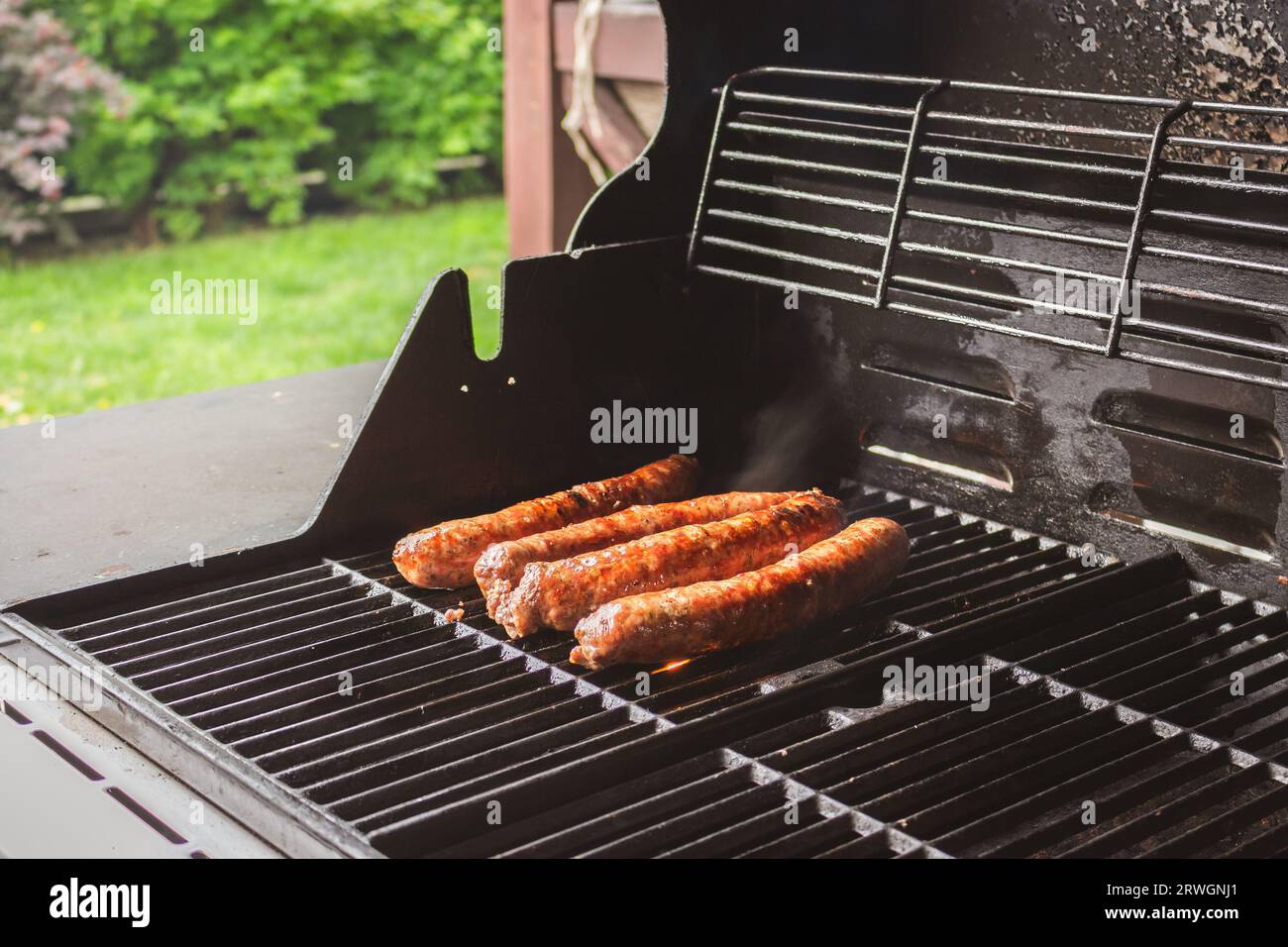 Sausages on the grill. Garden barbecue party. Pork sausages on the grill grate. Grilled bratwurst sausages. Picnic at backyard. Hot dog cooking. Stock Photo