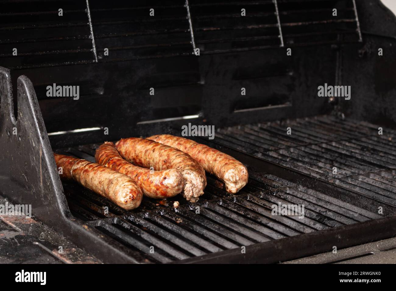 Sausages on the grill. Garden barbecue party. Pork sausages on the grill grate. Grilled bratwurst sausages. Picnic at backyard. Hot dog cooking. Stock Photo