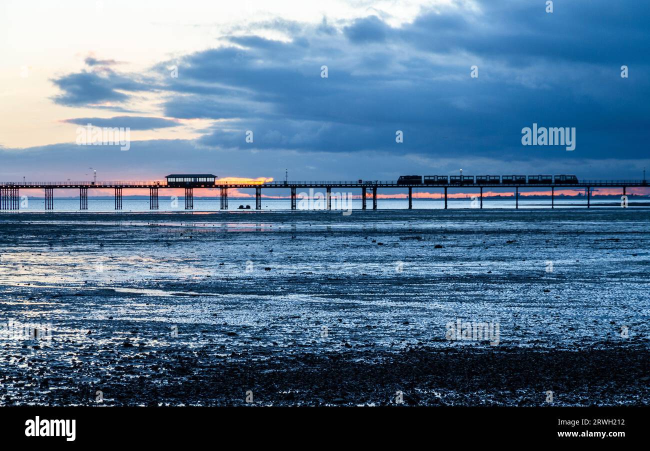 The pier at Southend in Essex at sunset. the tide is out and clouds roll in. Overall colour is blue Stock Photo