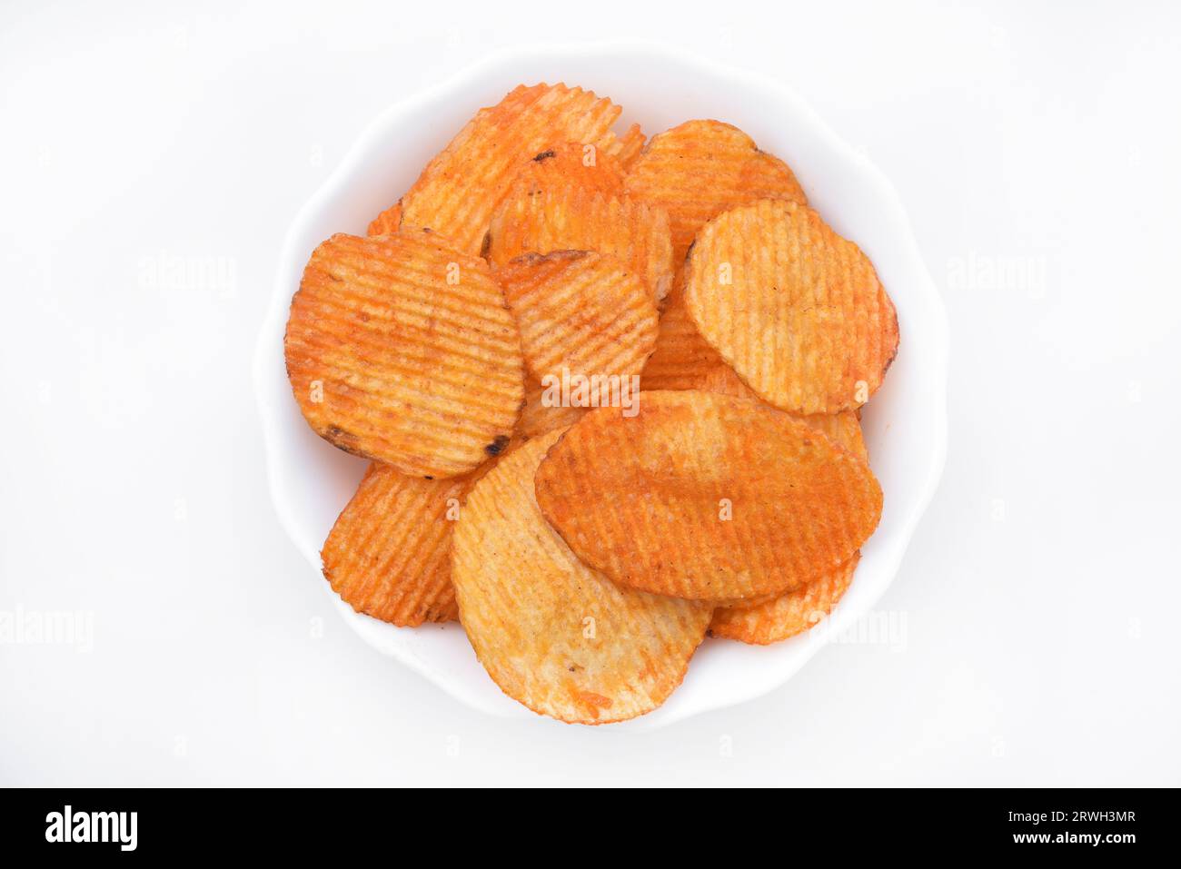 Red pieces of fried potatoes in a plate. Peppery chips on a white background. Stock Photo