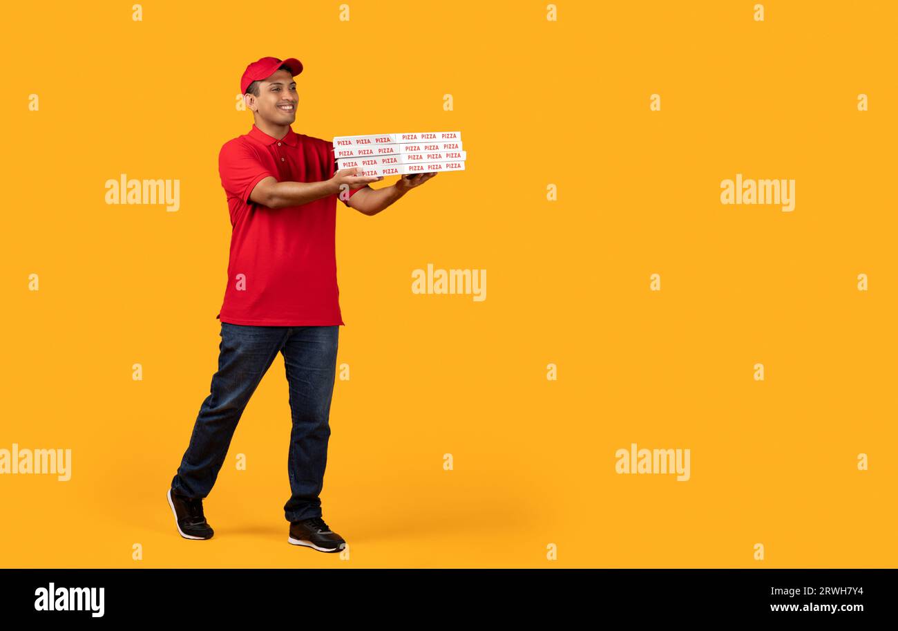 Middle Eastern Courier Holds Stack Of Pizzas Boxes, Yellow Background Stock Photo