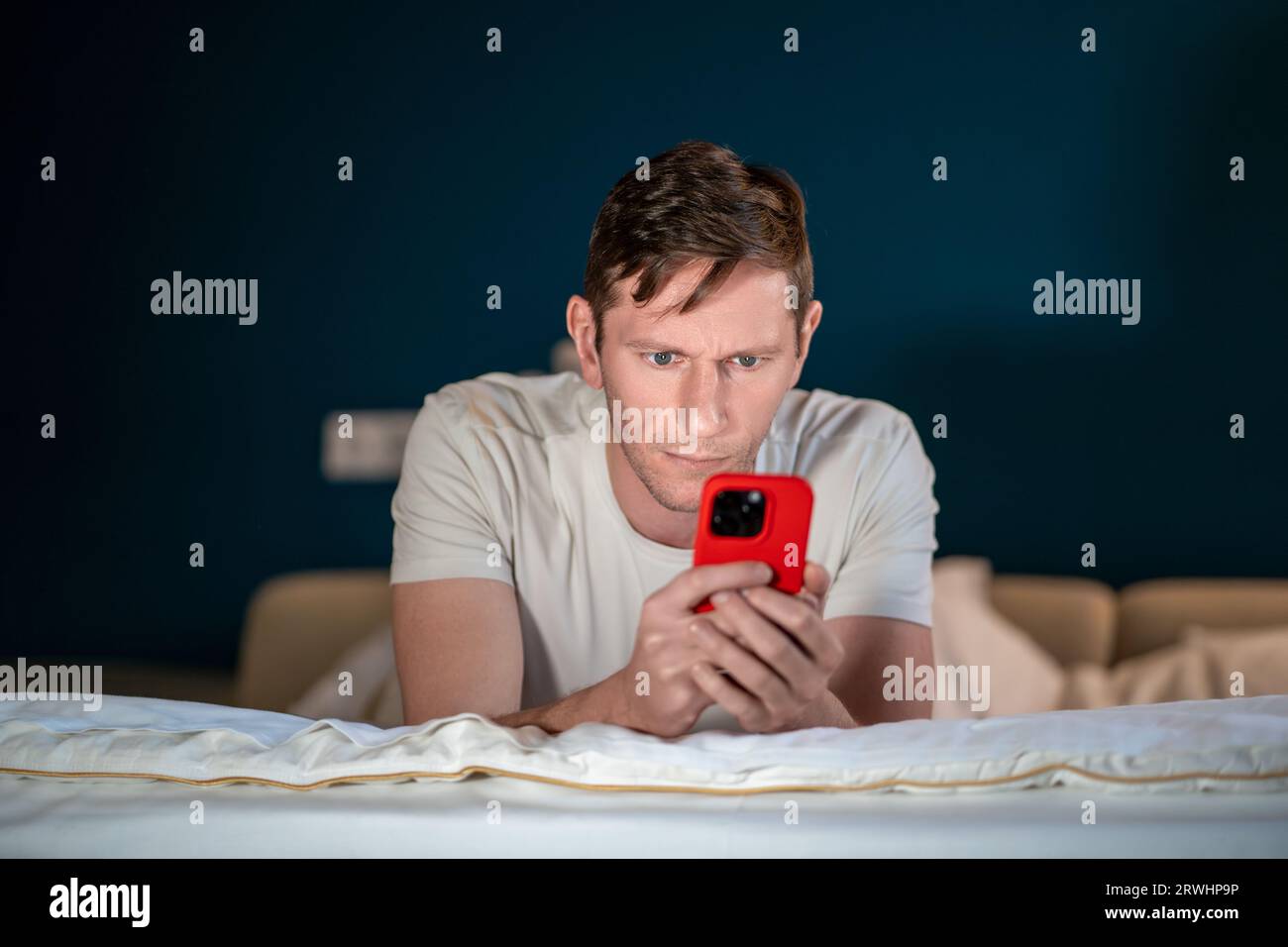 Man uses smartphone lying on bed. Online internet purchases solving business problems conducts chat Stock Photo