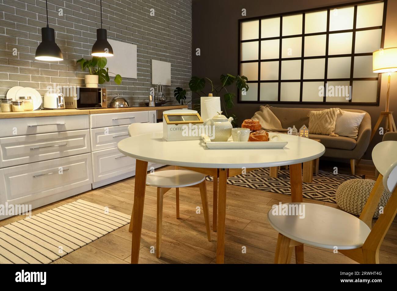 Interior of modern kitchen with glowing lamps, dining table, white ...