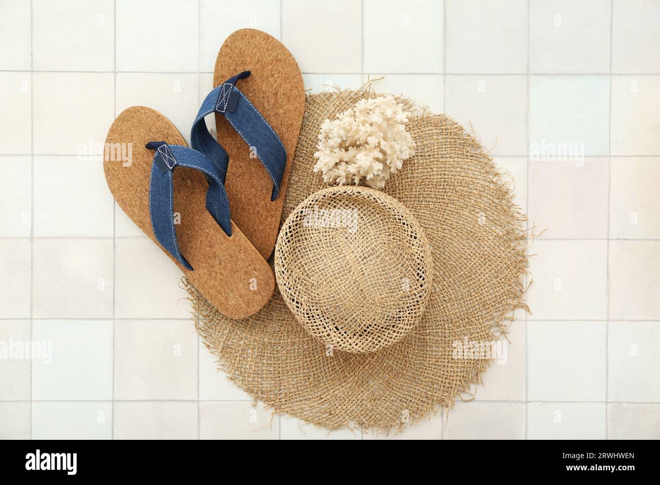 Pair of flip flops with straw hat and coral on white tile background ...