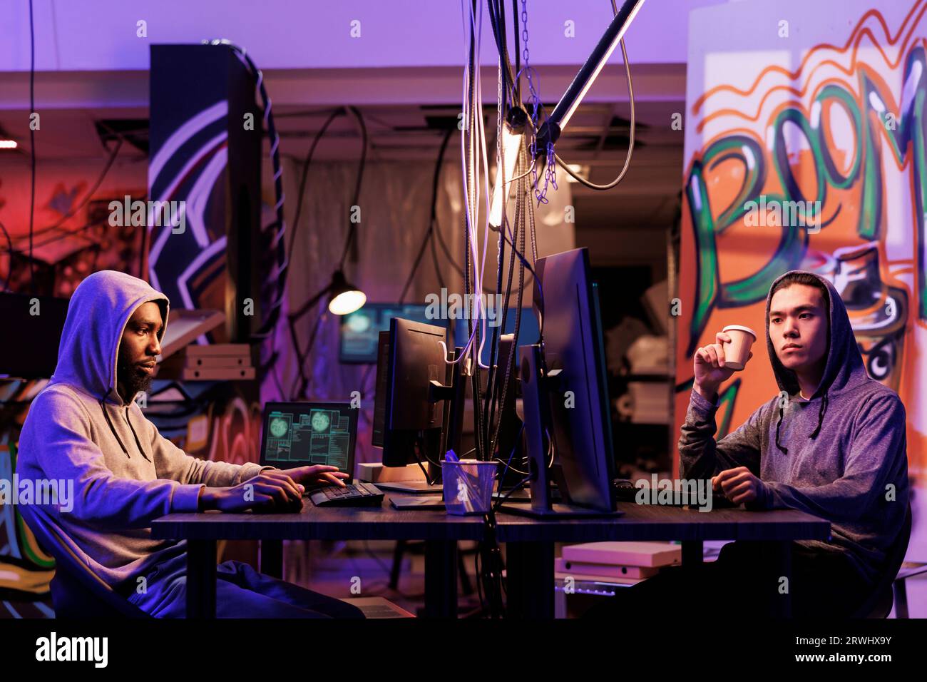 Hackers breaking into system and using spyware on computer while drinking coffee. Two criminals attacking website and programming internet virus malicious software at night Stock Photo