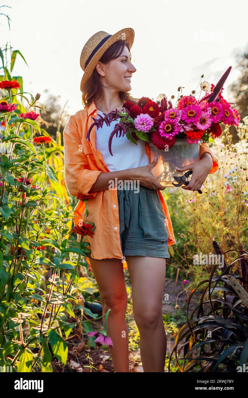 Portrait of woman farmer picking flowers in bucket in summer garden at