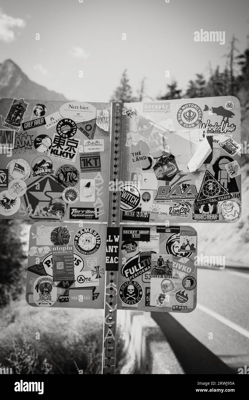 A roadsigns covered with stickers and decals.  The Duffy Lake road, between Lillooet and Pemberton BC, Canada.  Black and White Image. Stock Photo