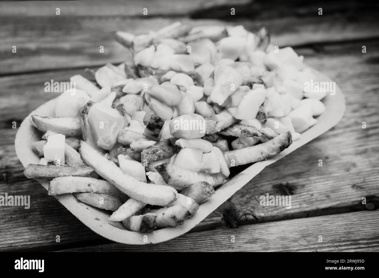 An order of poutine, a French Canadian dish of French fries, gravy, and cheese curds, at a stake street food stand.  Black and white image. Stock Photo