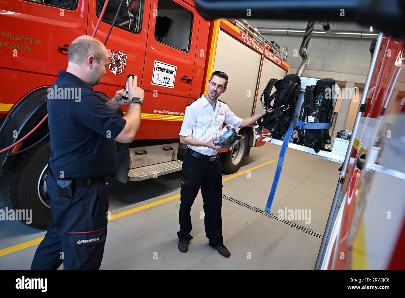 PRODUCTION - 11 September 2023, Baden-Württemberg, Weingarten In Württemberg: Alexander Binder (r), deputy commander of the Weingarten fire department, and squad leader Matthias Burkhardt shoot a short video clip for Instagram in the vehicle hall. The Weingarten Fire Department has more than 10,000 Instagram followers and is looking for members via social media. Photo: Felix Kästle/dpa Stock Photo