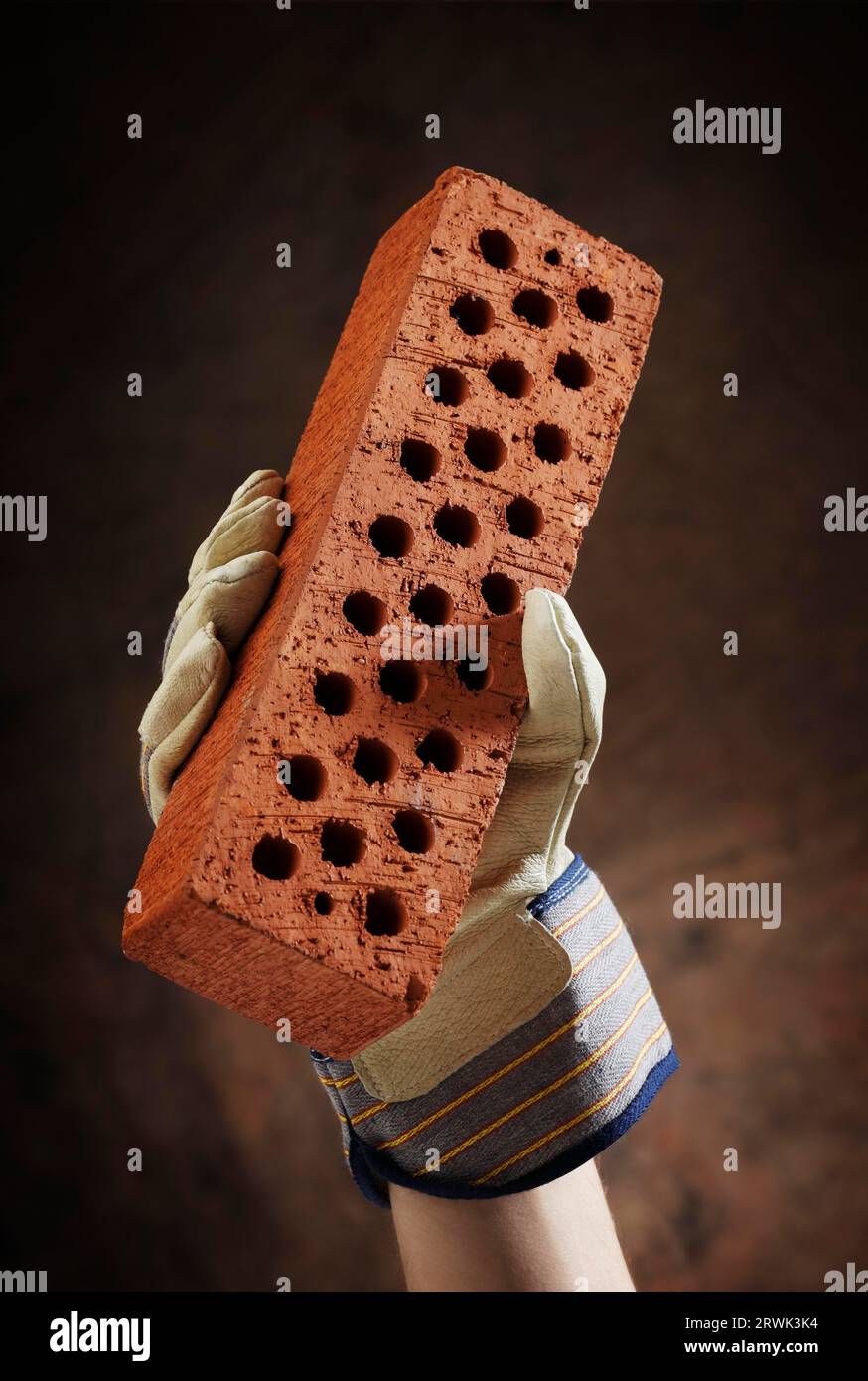 A gloved hand holding a perforated brick Stock Photo