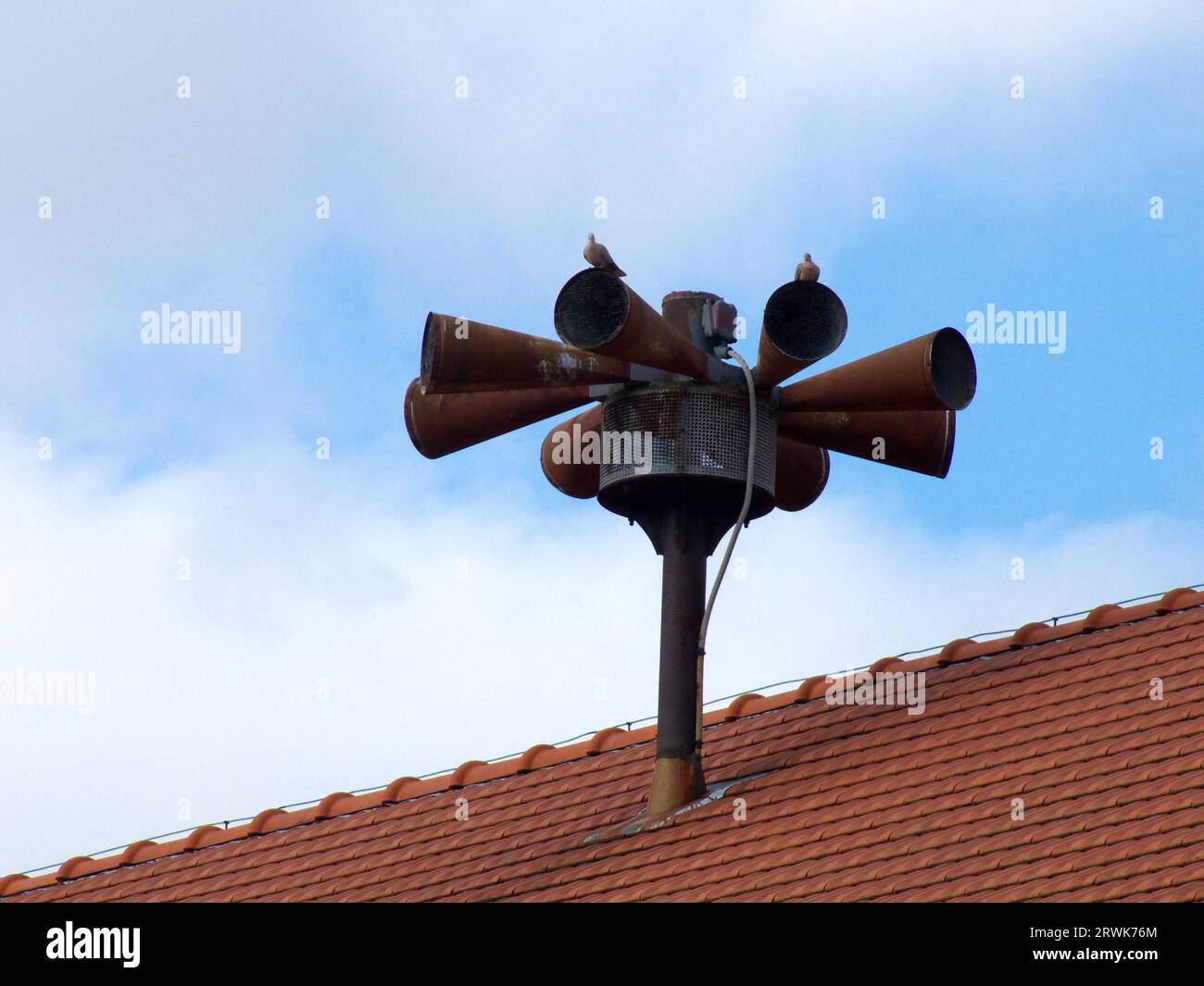 Older, already rusty siren, on a house roof, background blue sky Stock Photo