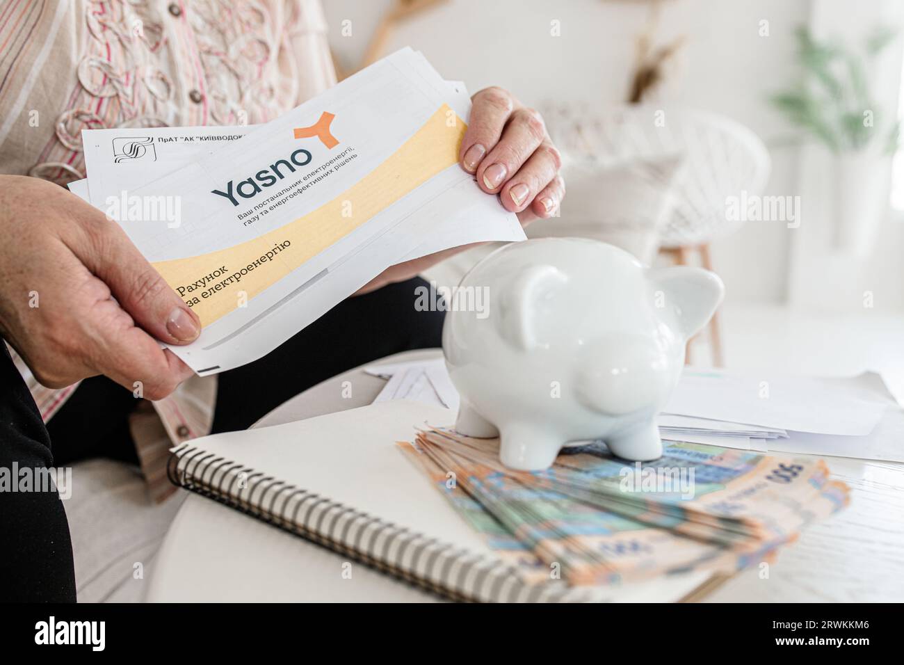 Kyiv, Ukraine - April 07, 2023: Electricity bill from Yasno and Kievvodokanal. Economic challenges in Ukraine: Elderly woman grappling with electric Stock Photo